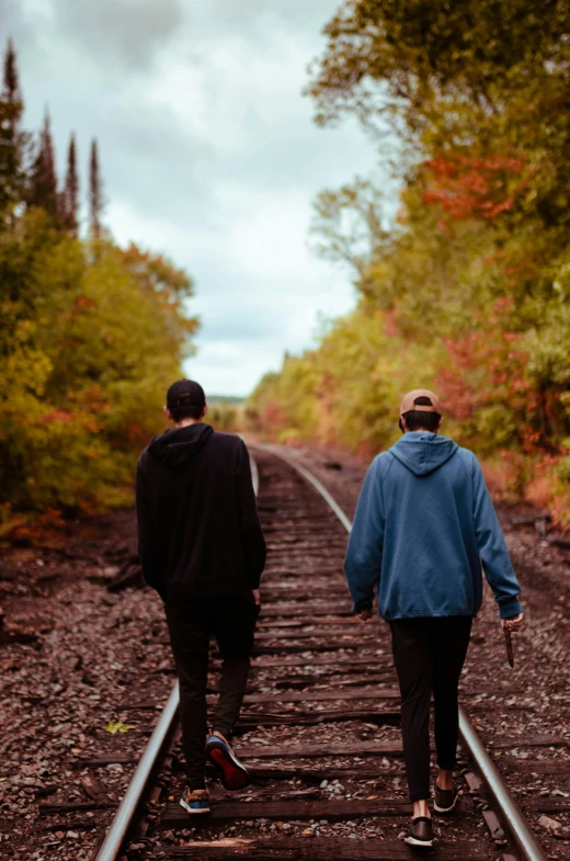 two men walk down train tracks in the woods