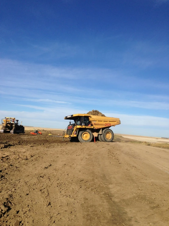 two large tractors are in the dirt with blue skies