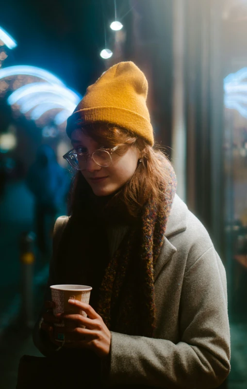 a woman with glasses and a knitted hat holding a cup