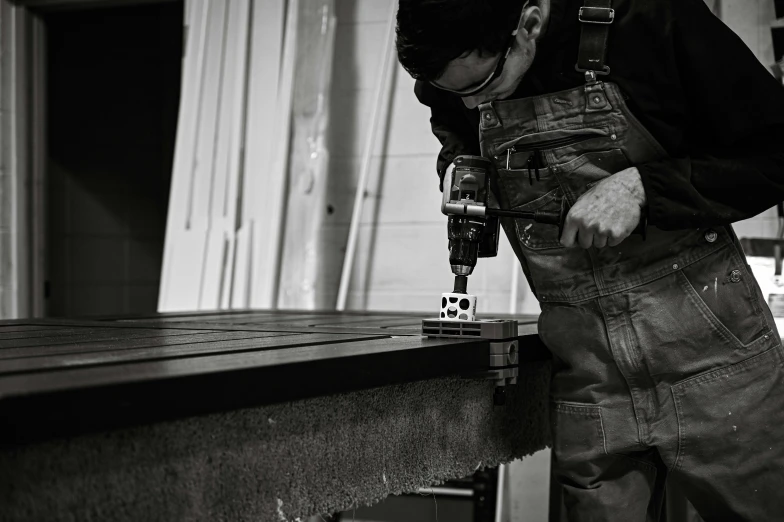 a man in overalls is drilling a piece of metal