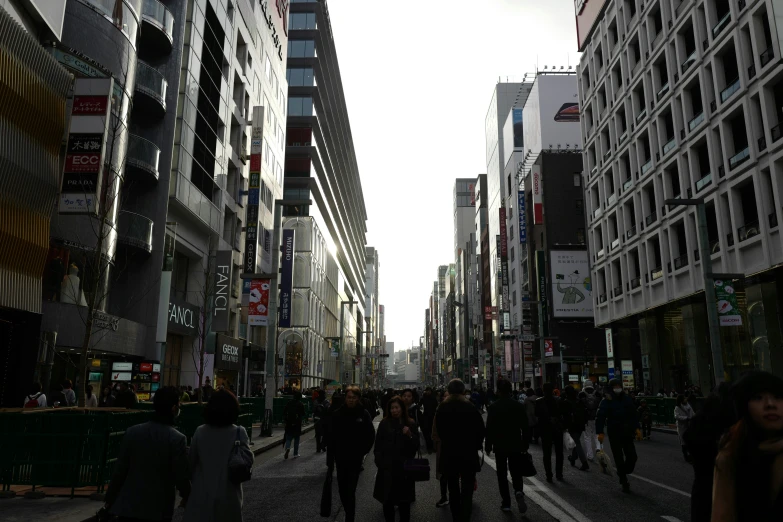 people are walking through a city street while buildings loom