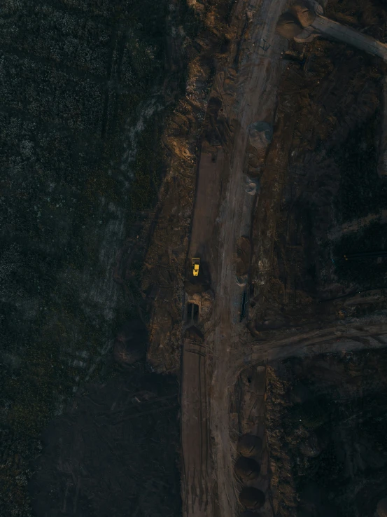 the aerial view of a dirt road with forest in background