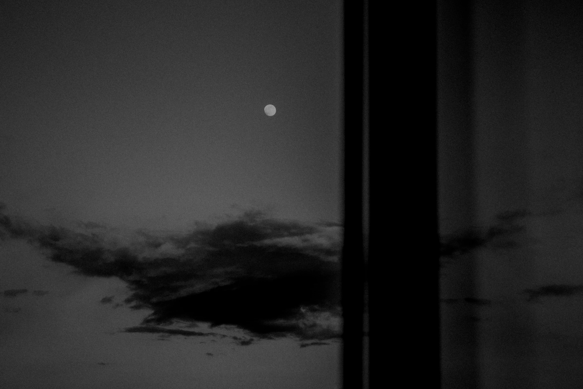 the moon seen through a window with clouds and fog