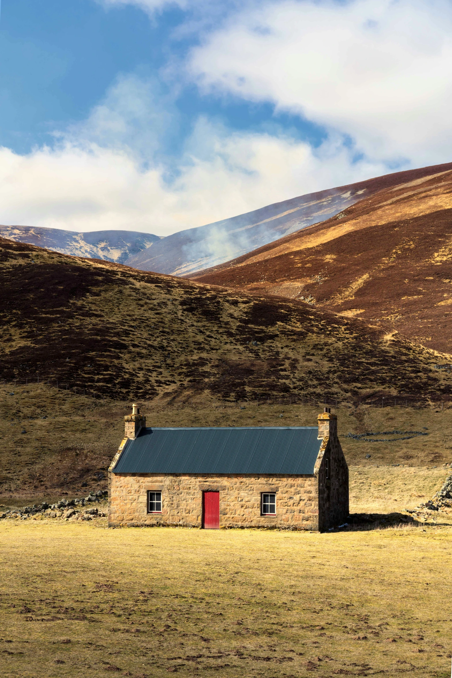 a small stone house with red doors in the hills