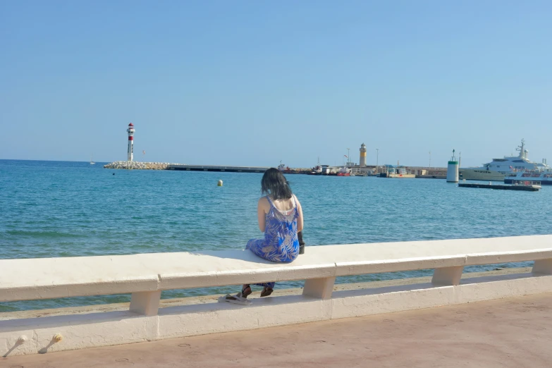 a girl sitting alone on a wall looking at the sea