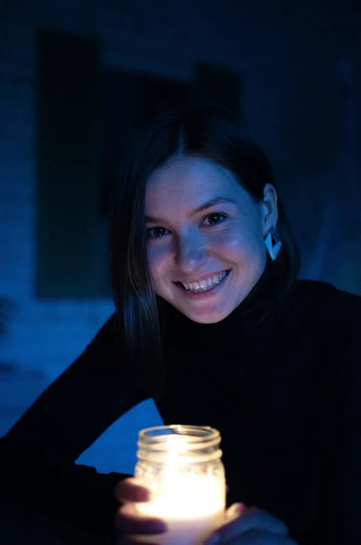 a woman smiling in the dark holding a lit jar