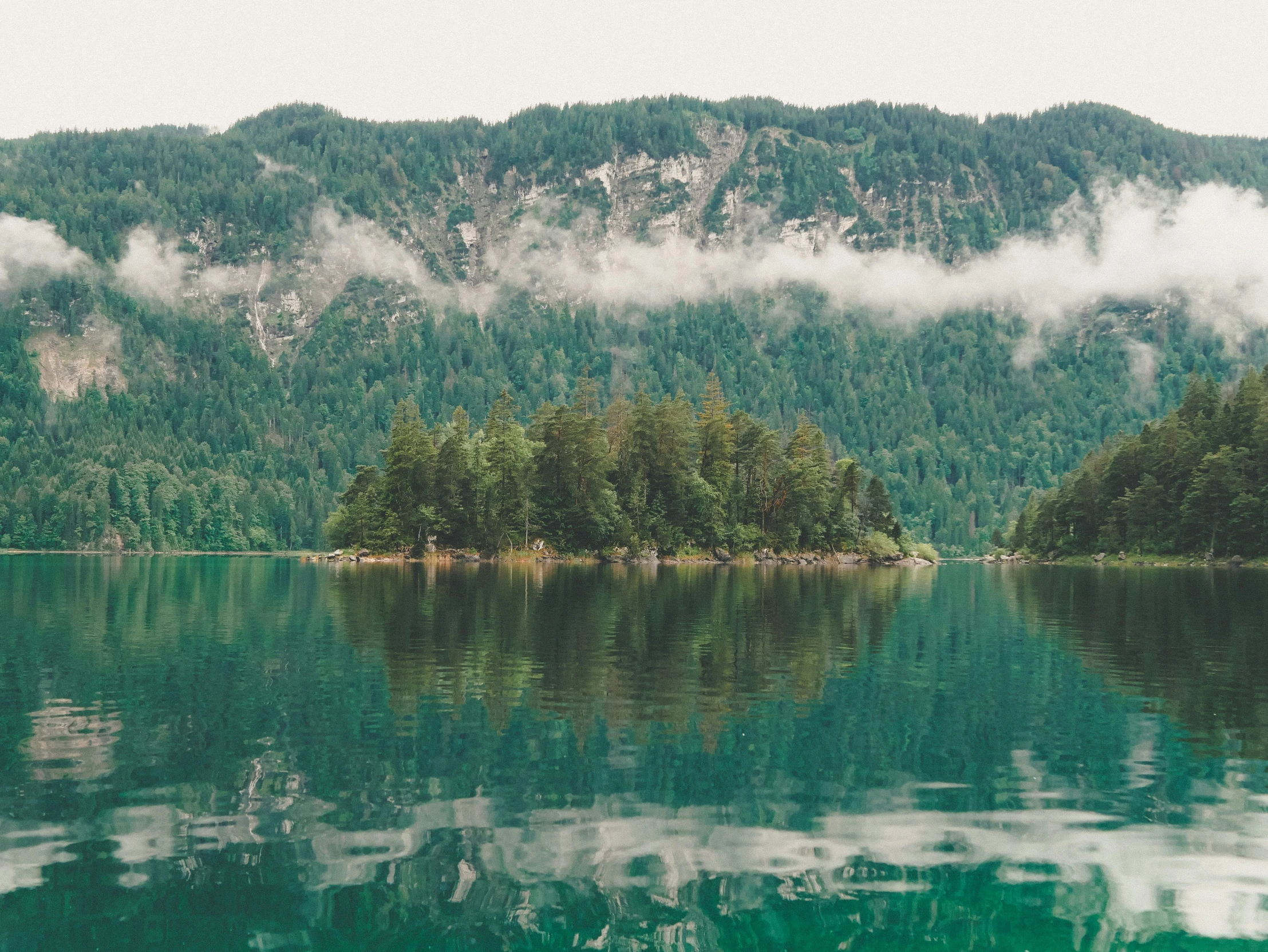 fog hanging over mountains and trees reflected in the water