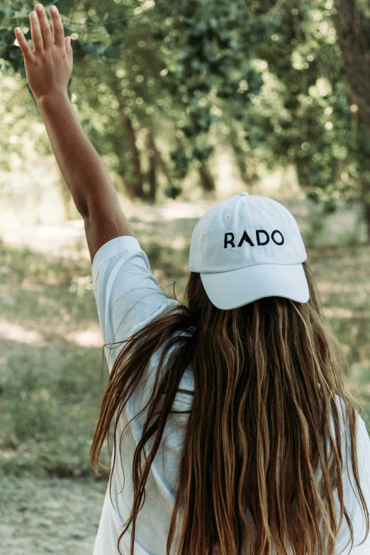 a woman with long hair and a cap raising her hands up