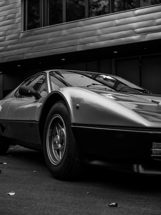 a man in a suit leans against the back of a parked sports car