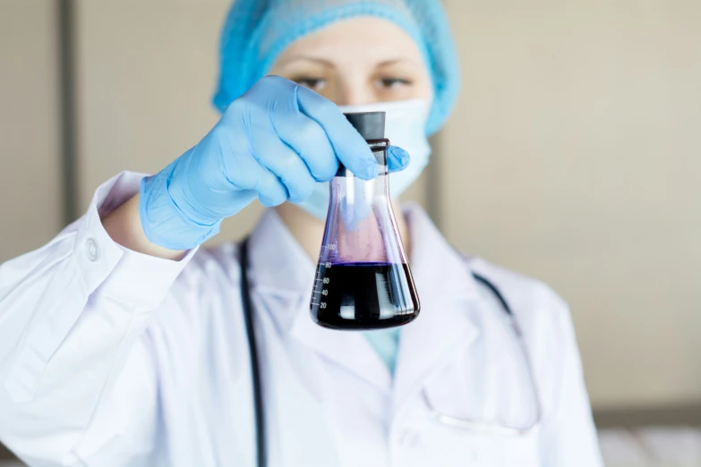 a woman in white coat and cap holding up a tube with black liquid