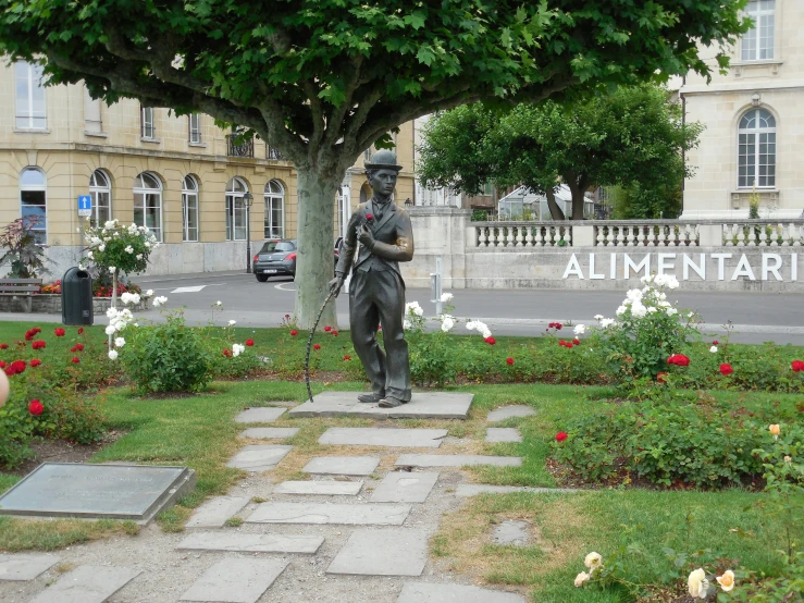 a statue sitting in a park next to a flower bed