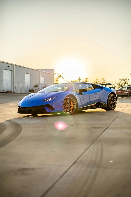 blue sports car parked on a cement surface with sunset behind it