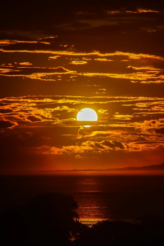 sun setting with dark clouds and orange color over water