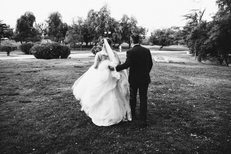 the bride and groom are walking on the grass in black and white