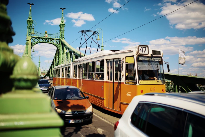 yellow bus moving on a city street by a green bridge