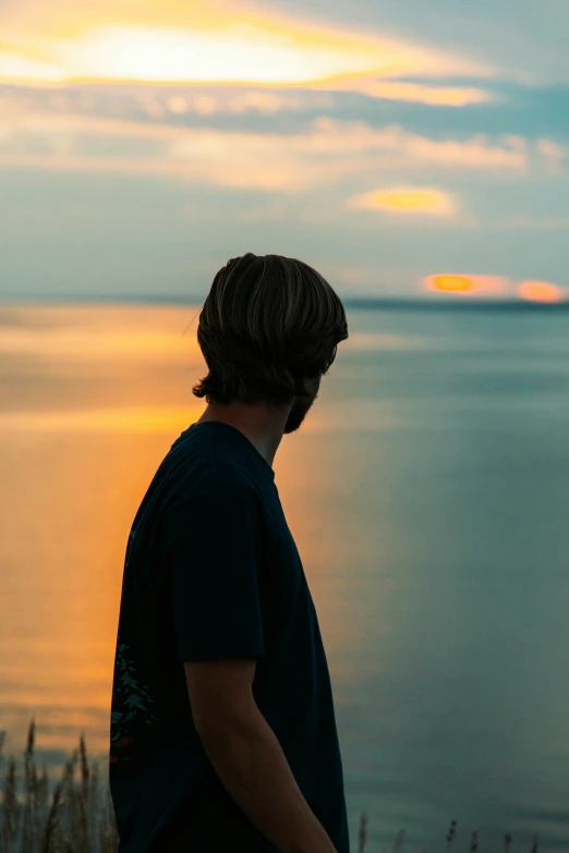 a boy is looking out over the ocean at sunset