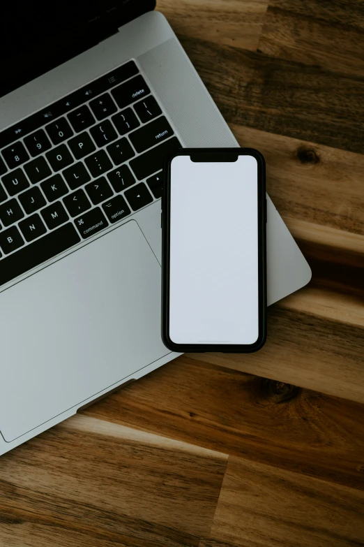 a smart phone and a laptop on a wooden surface