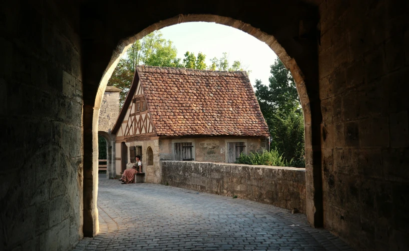 a building with red clay roofs and cobblestones as seen through an archway on a brick road