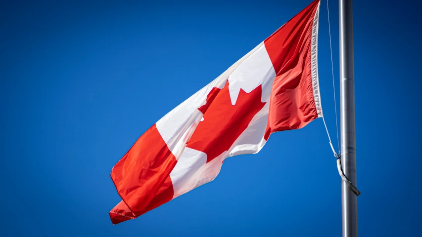 a canadian flag is flying on the wind with blue sky