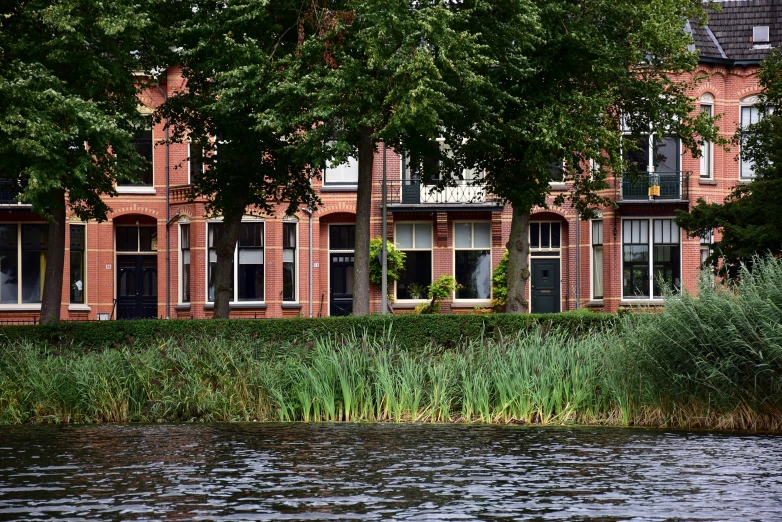 a brick building with windows near the water and trees