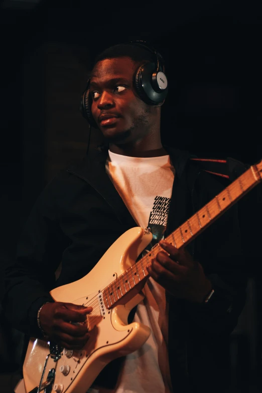 a black man in headphones plays a white guitar