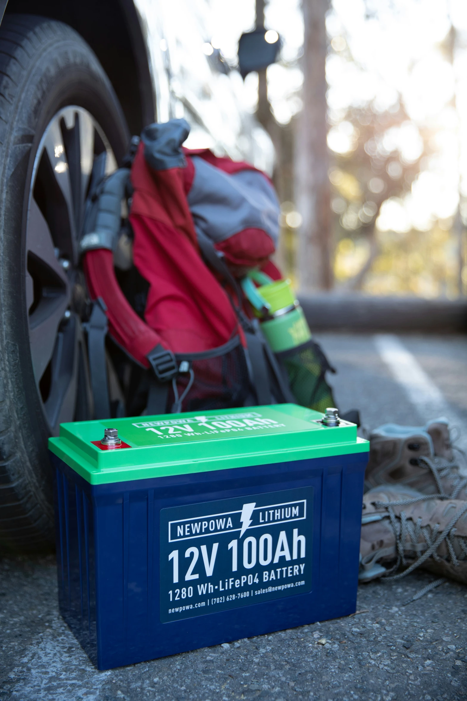 a camping blanket, backpack and an agam battery next to a tire