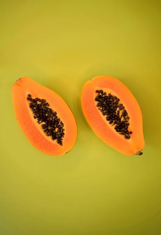 two pieces of orange fruit with some black seeds on top