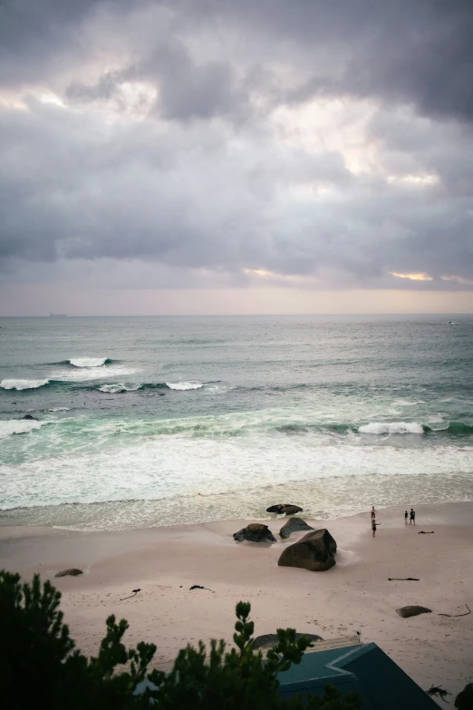 a beach with two people and many rocks near water