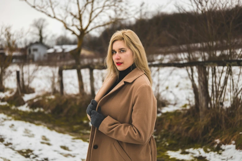 a beautiful blond woman standing in a field with trees