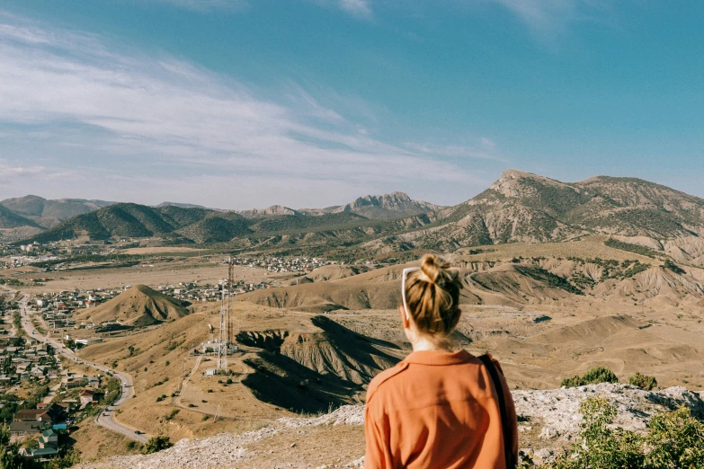 a woman in orange sweater standing on top of a cliff