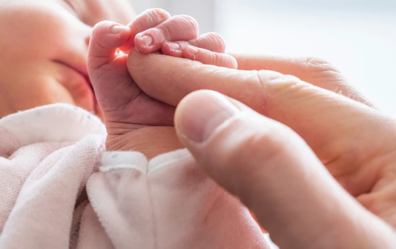 a person's hand holding an infant's hand and touching the fingers of someone