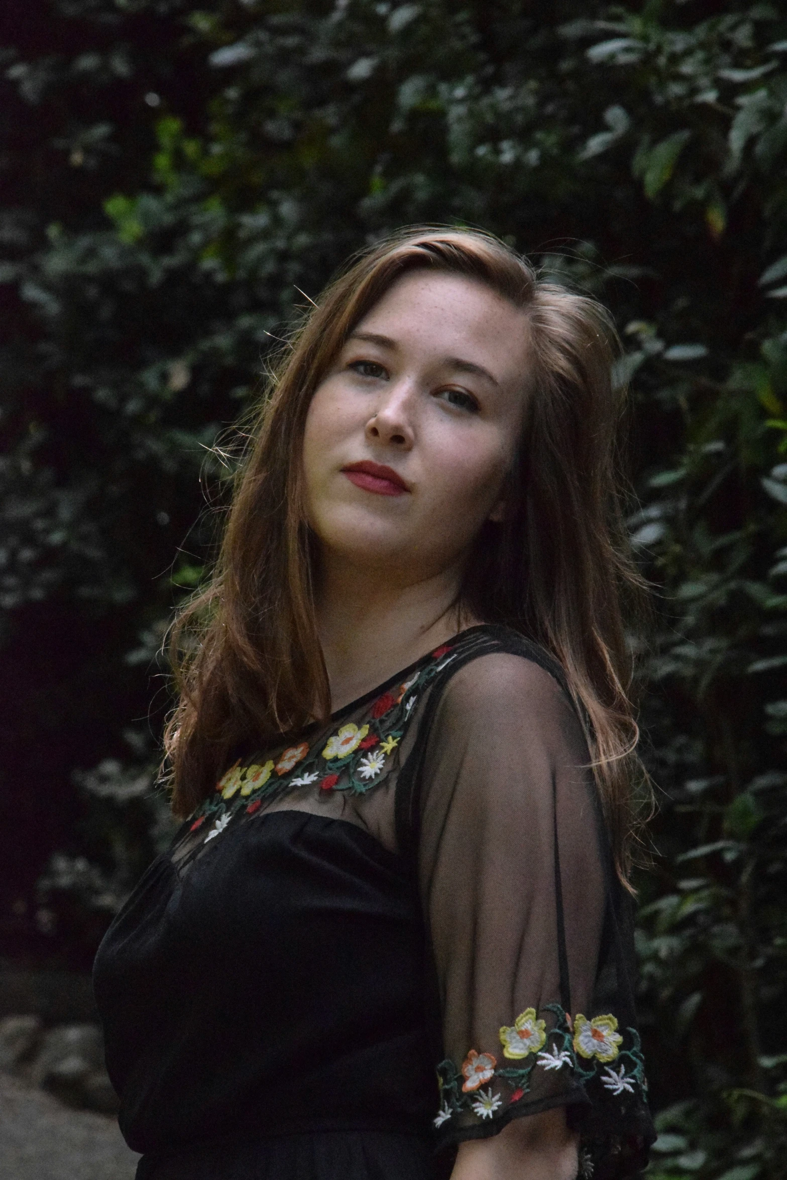 a woman standing next to a bush while looking off into the distance