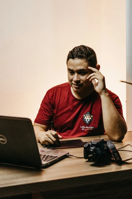 a man sitting at a table holding a cell phone and looking at his laptop