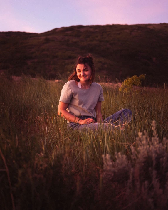 a smiling girl sits alone on the field in grass