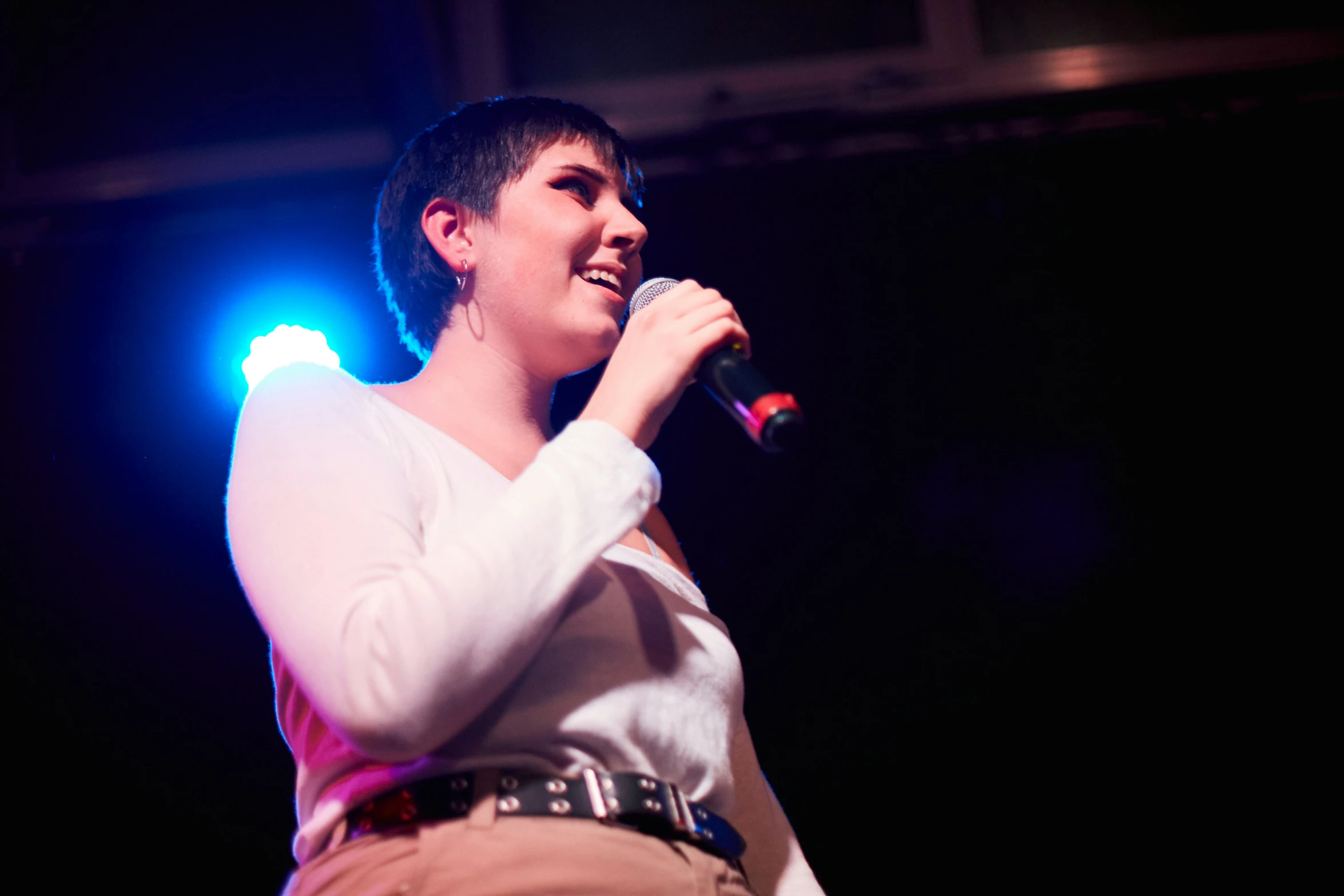 a woman with short hair and lights on her face sings