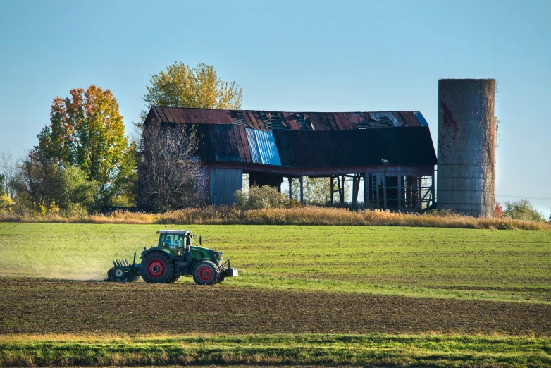 the tractor is driving through the field behind the building