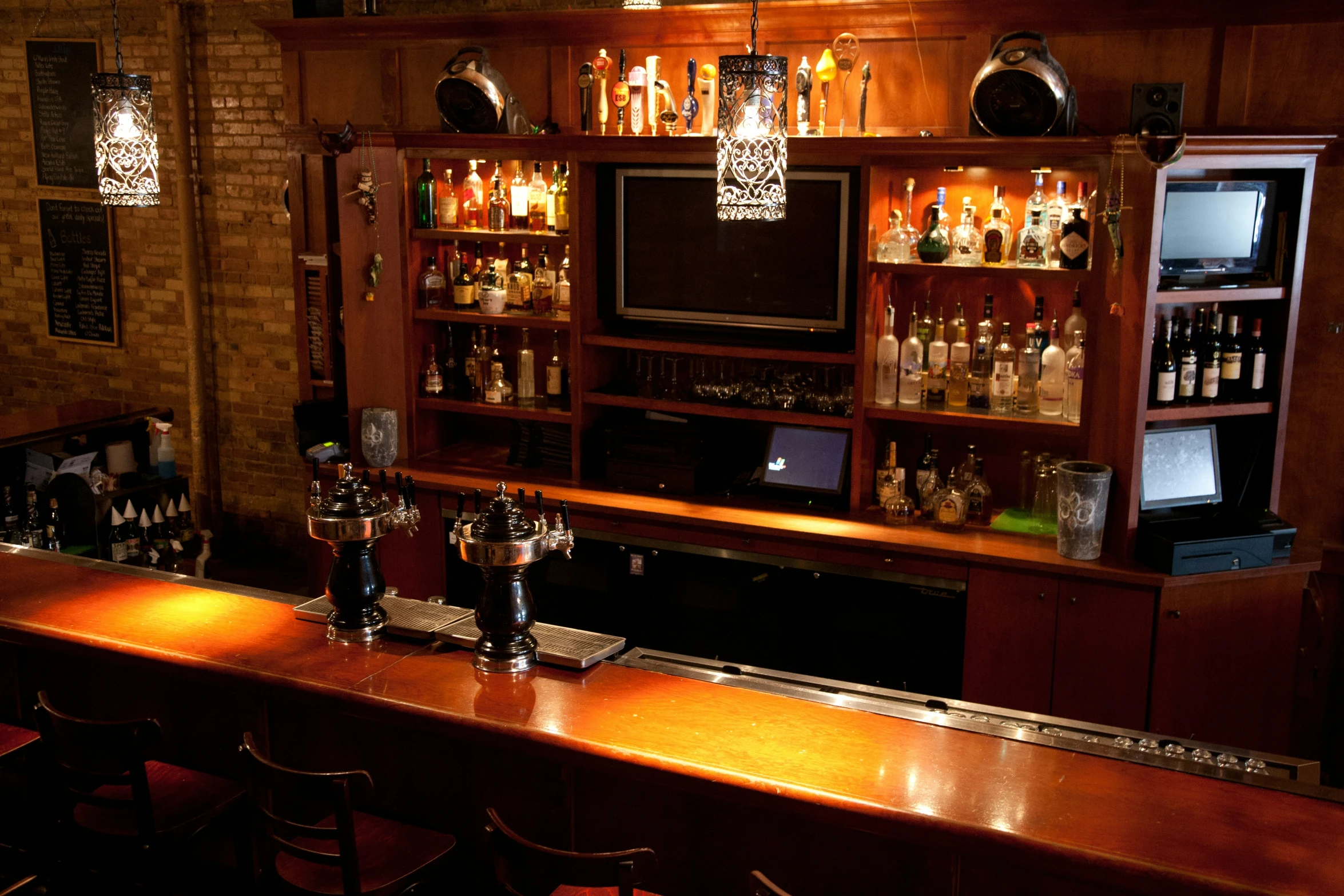 a bar with lights over it and liquor bottles in the back