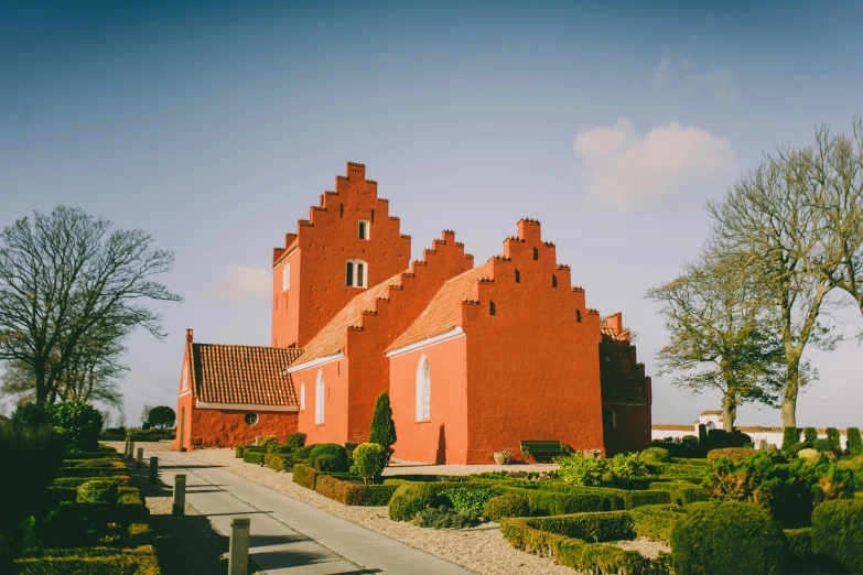 a long red building with three towers next to bushes