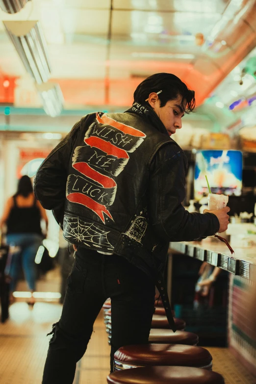 a man in a leather jacket sitting on a stool with a painting on his jacket