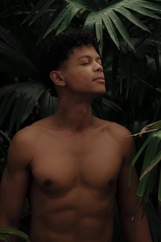 a young man posing for a picture in front of jungle leaves