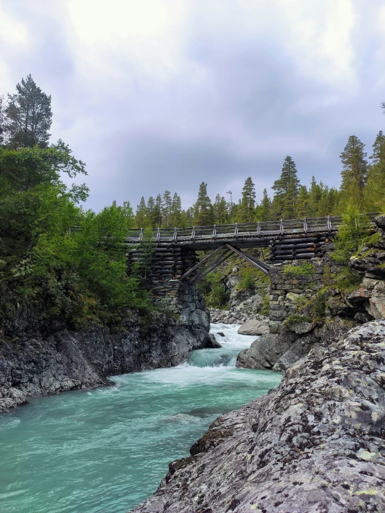 a mountain stream is flowing below an old bridge