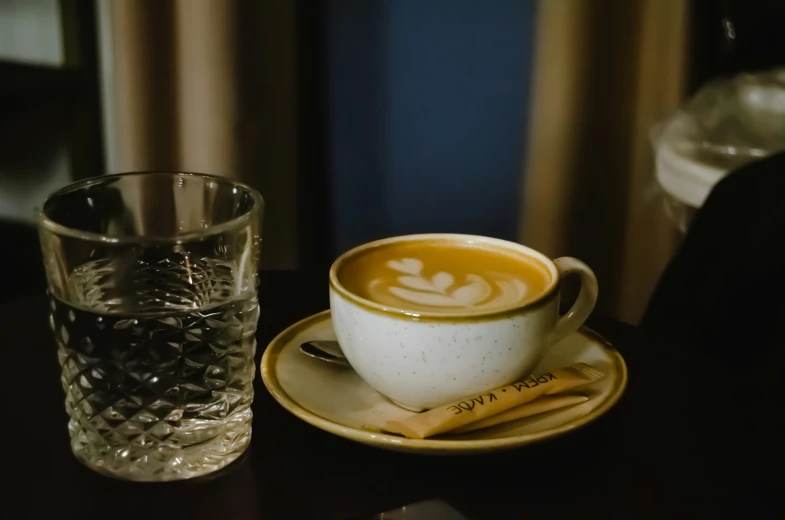 the coffee cup is sitting on the saucer near a drink glass