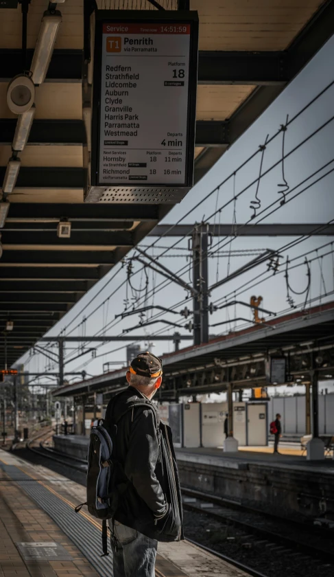 a man with a backpack standing in a train station waiting for the train