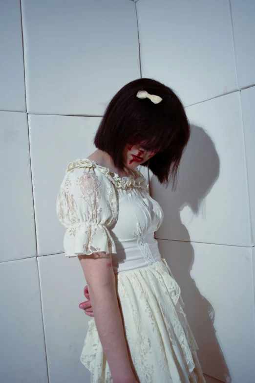 woman standing in white dress with her head against the wall