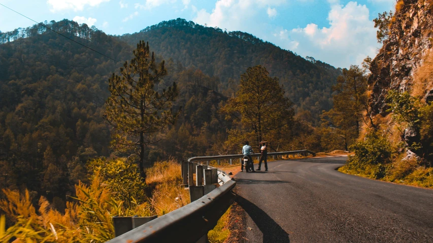 a man and woman stand on a paved road in front of hills