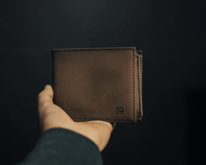 a hand holding a leather wallet over black background