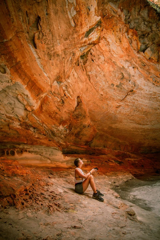 a young man sitting on the beach next to a cliff