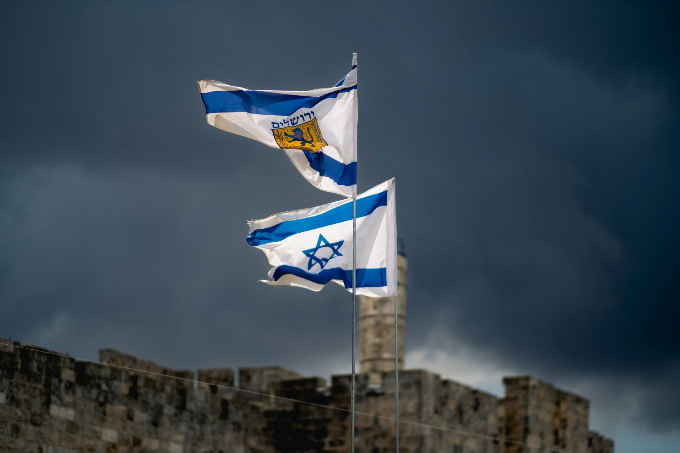 flags with flag poles attached against an old stone wall