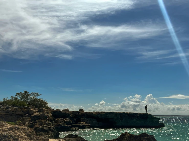 a kite flying in the air over a rocky cliff with blue water