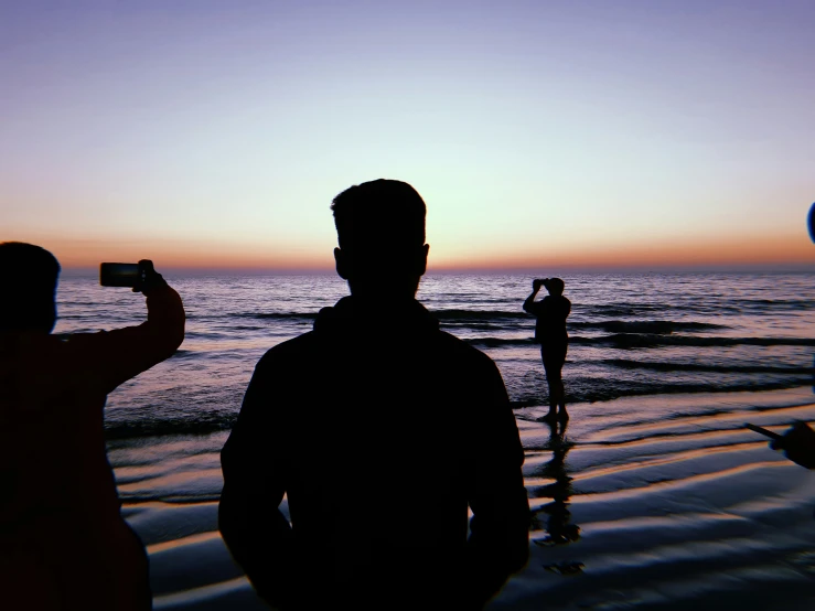 two people on the beach watching a woman take pictures